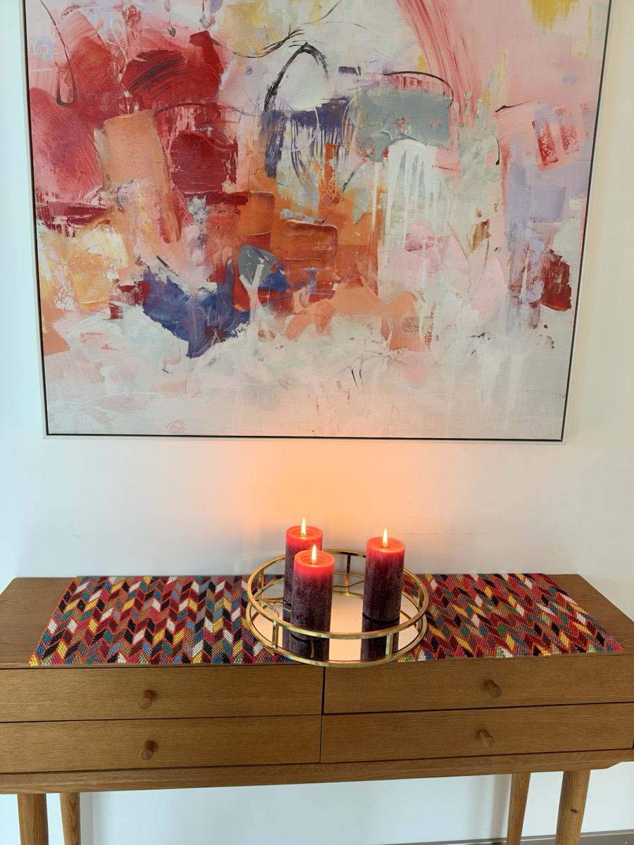 Maroon Winds on a wooden console with candles, under a painting